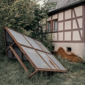 Rustige, beschädigte Blechgarage in verwildertem Garten, verwaschene Stelle am Boden deutet auf mögliche Abwasserprobleme hin.