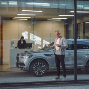 Mann übergibt Autoschlüssel vor einer modernen Bankfiliale mit einem deutschen Mittelklassewagen.Mann übergibt Autoschlüssel vor einer modernen Bankfiliale mit einem deutschen Mittelklassewagen.Mann übergibt Autoschlüssel vor einer modernen Bankfiliale mit einem deutschen Mittelklassewagen.