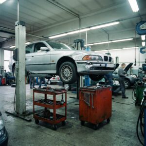 Ein PKW mit deformierter Stoßstange und verbeultem Kotflügel steht auf einer Hebebühne in einer Werkstatt.