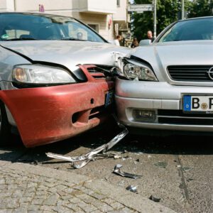 Frischer, glänzender Blechschaden überlagert eine matte, alte Delle an der verkeilten Front zweier Fahrzeuge.